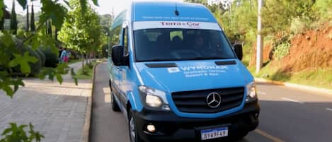 Una camioneta azul con la marca 'Terra e Cor' y 'WYNDHAM Gramado Termas Resort & Spa', estacionada en una calle bordeada de vegetación.