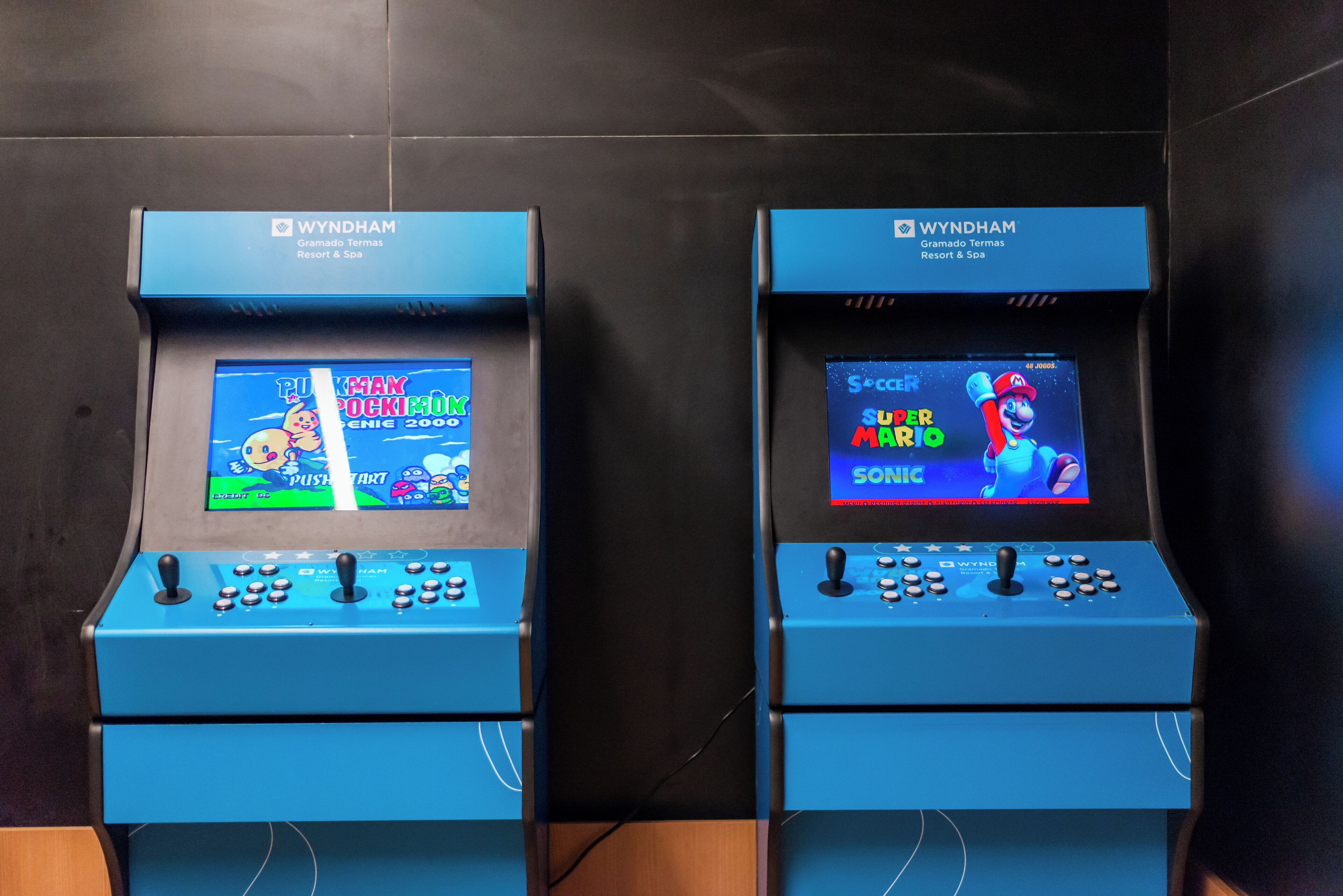 Dos estaciones de videojuegos azules en Wyndham Gramado Termas Resort & Spa, con juegos como 'PUSH START' y 'SUPER MARIO'.