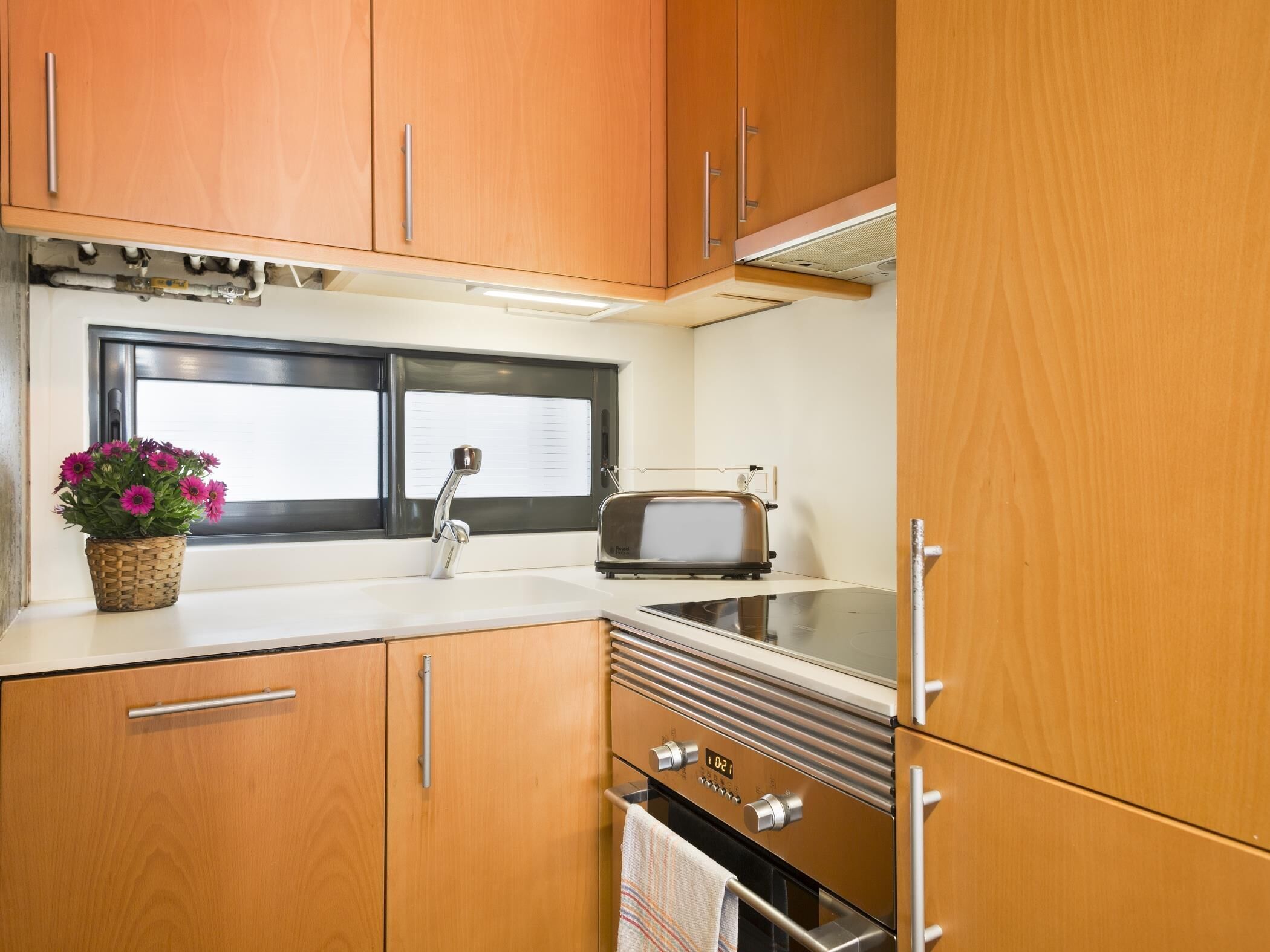 A compact kitchen with wooden cabinets, a built-in sink, a toaster, and a stove.