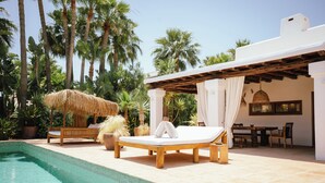 A poolside area with a lounge chair, a thatched umbrella, and a dining set.