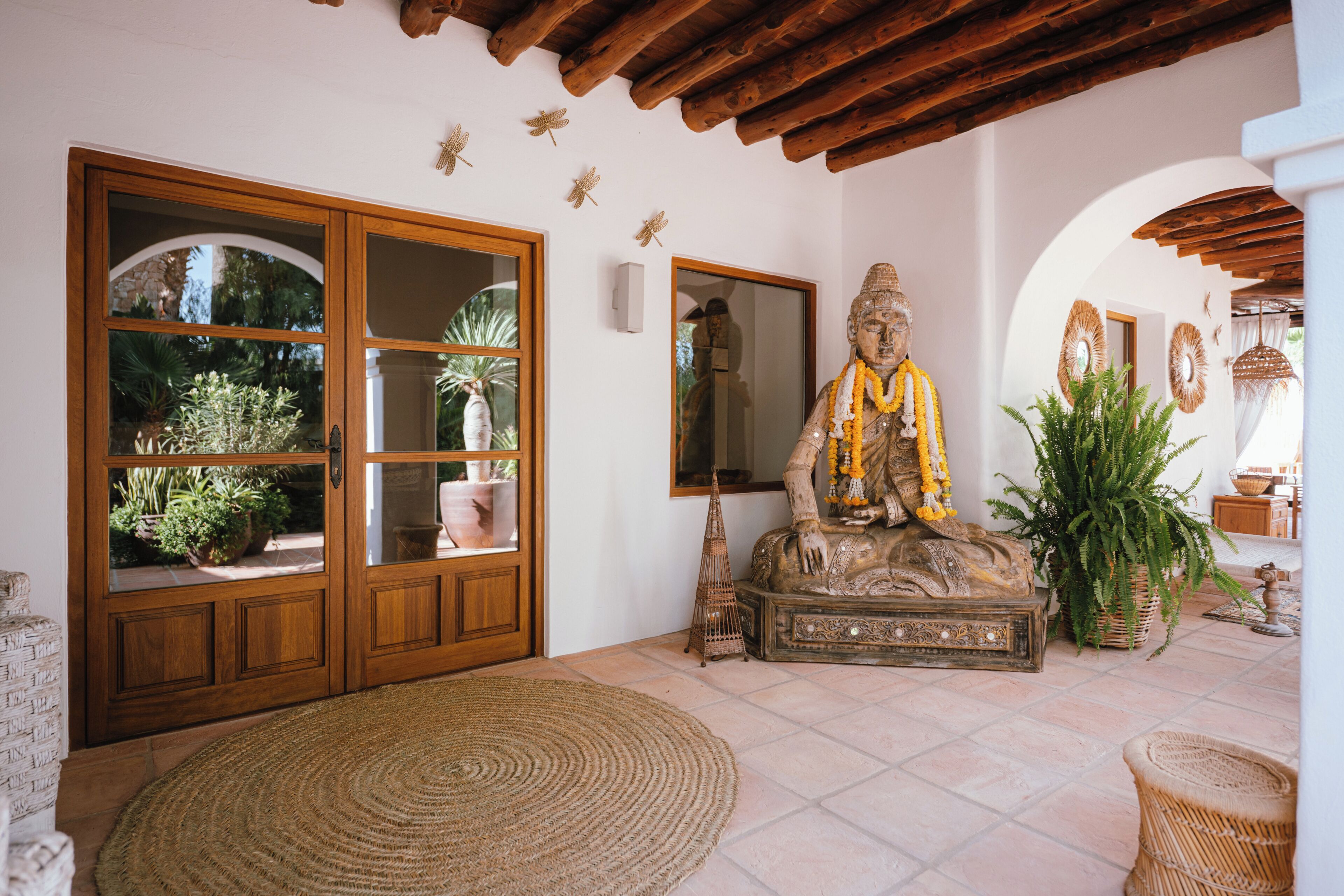 Une pièce avec une porte en bois, une statue, un tapis tissé et des plantes en pot.