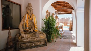 A statue of a seated figure with intricate carvings, a large mirror, and a potted plant in a hallway with an arched ceiling.
