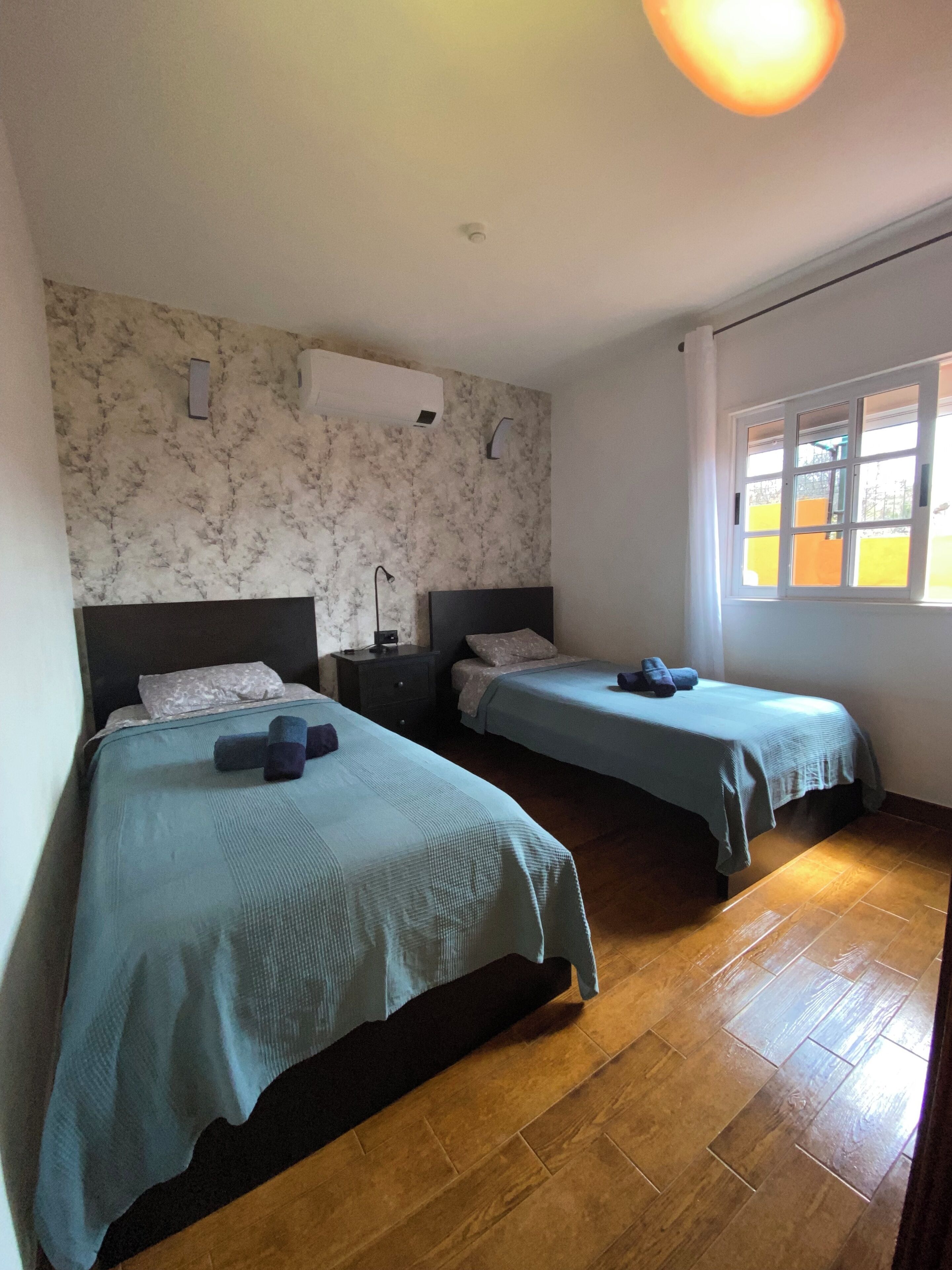 Ein Schlafzimmer mit zwei Betten, einer Wand mit Marmormuster, einer Deckenleuchte und einem Fenster mit Blick.