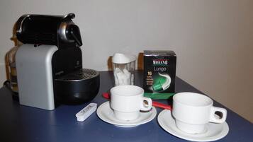 Une machine à café, deux tasses, une boîte de capsules de café et un sucrier sur une table.
