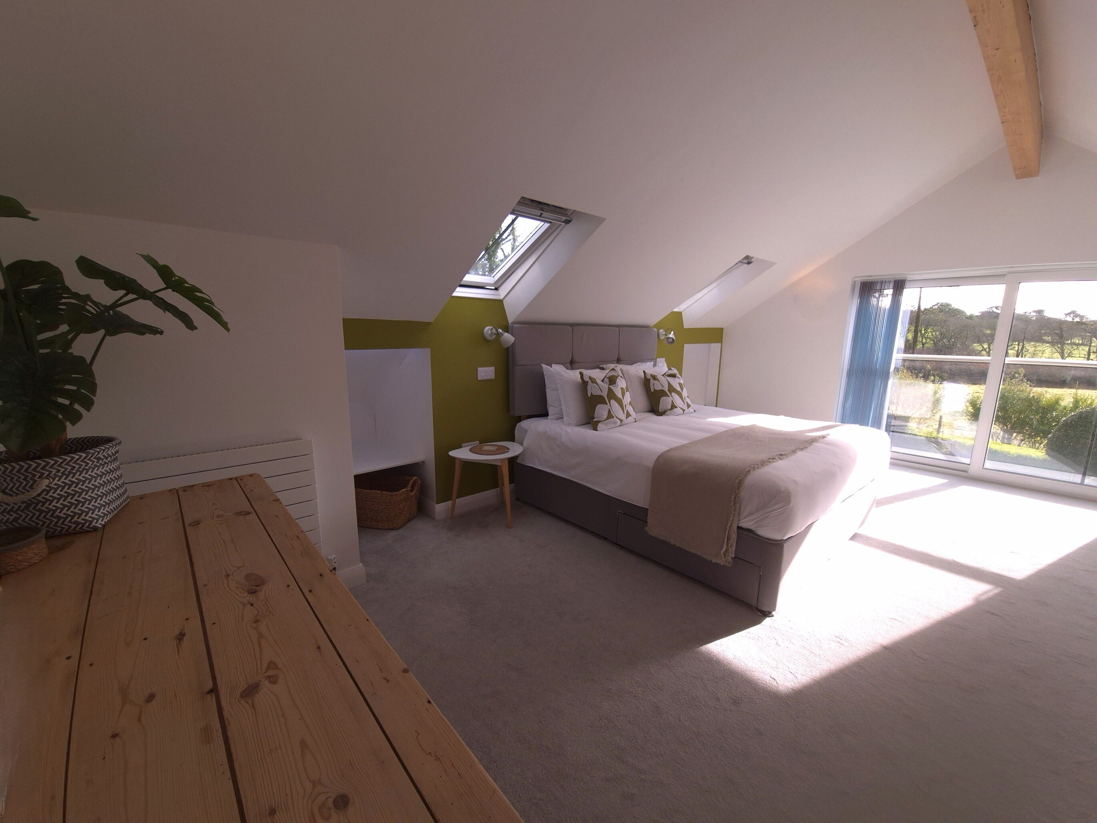 A bedroom with a sloped ceiling, a skylight, a bed with pillows, a bedside table, and a potted plant.