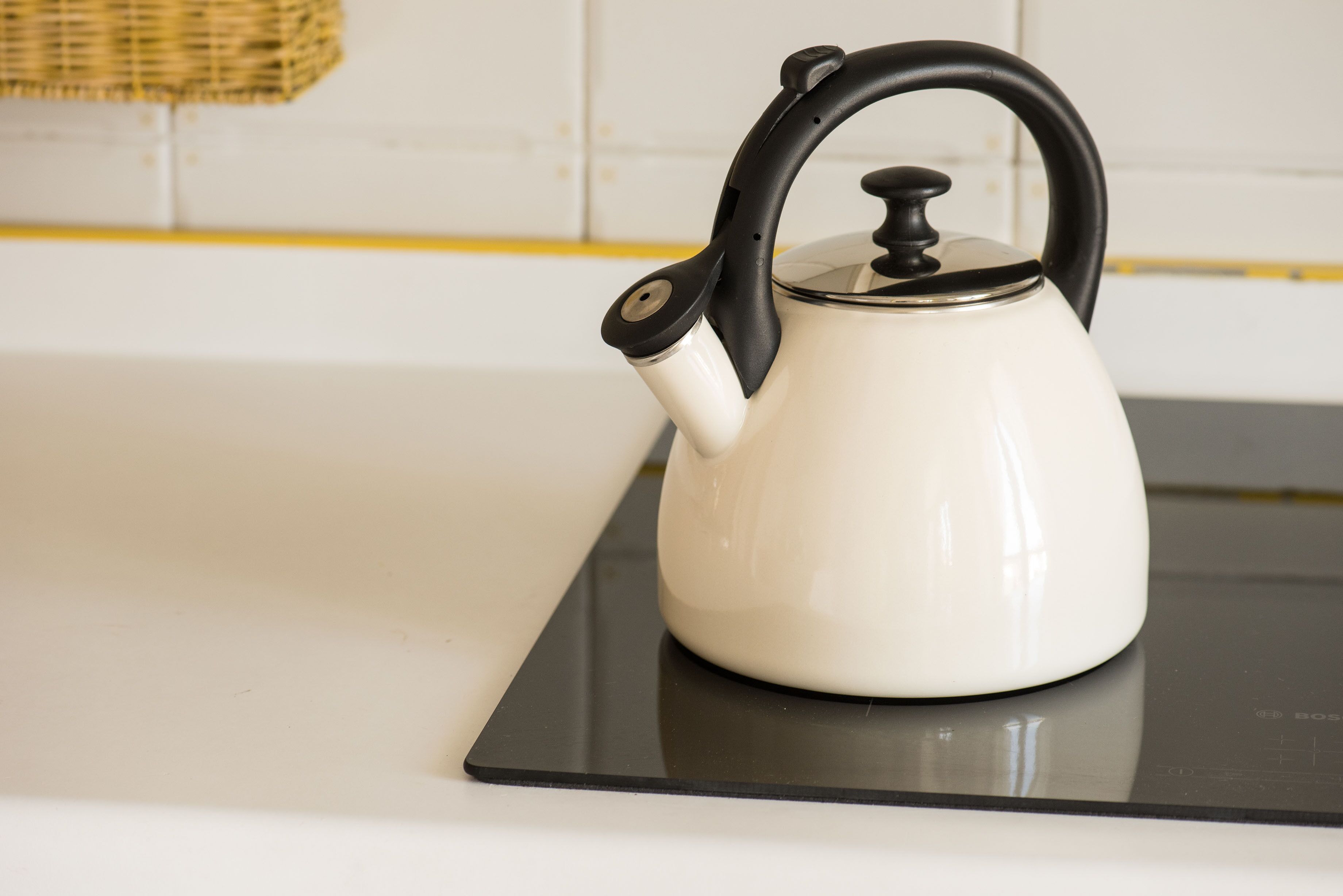 A white kettle with a black handle on a black stovetop in a kitchen.