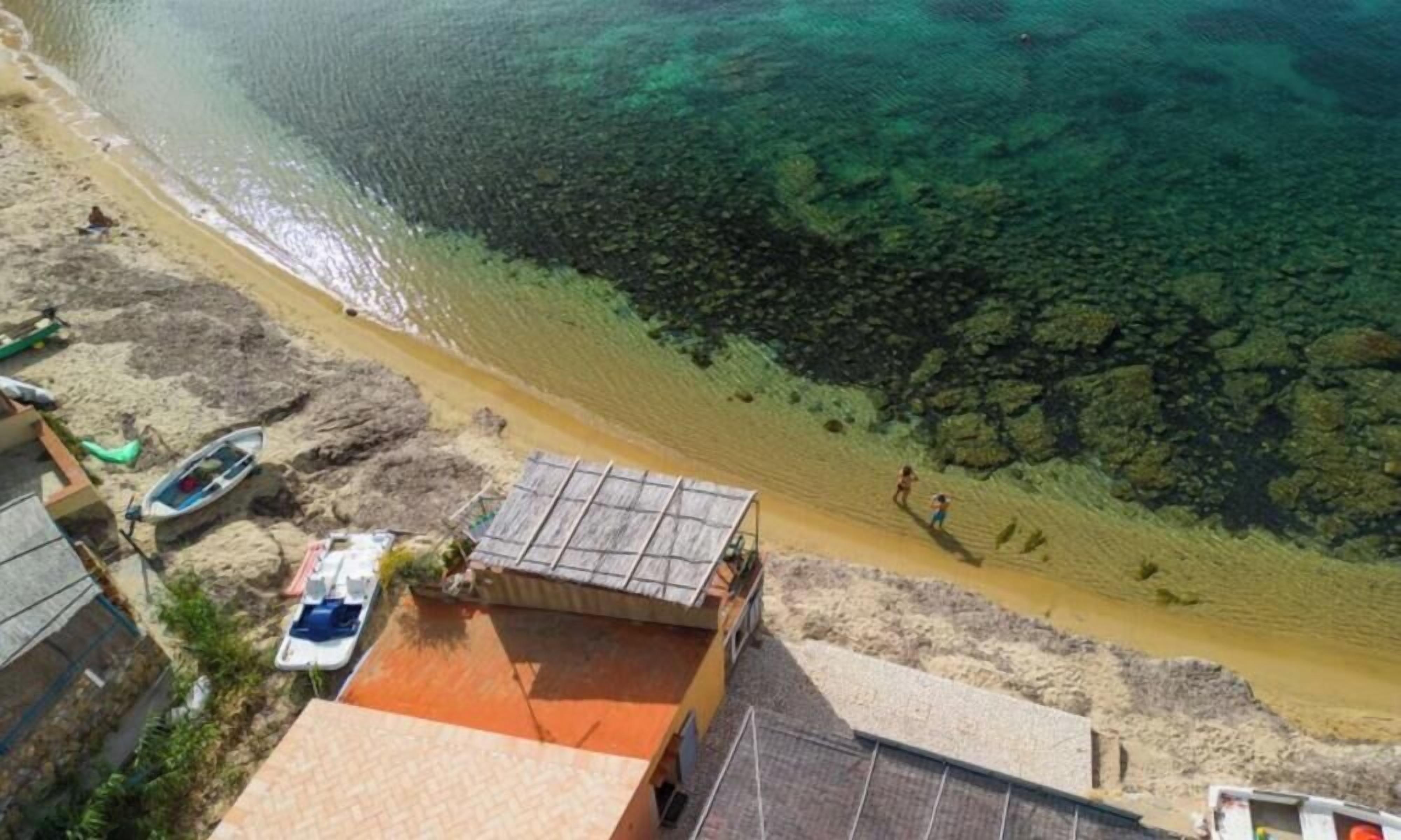 Ein Strand mit klarem Wasser, einem Boot und einem kleinen Gebäude.