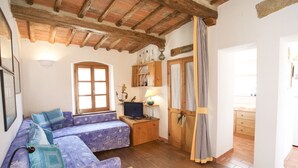 A cozy room with a wooden ceiling, a sofa with patterned cushions, a small table with a lamp, and a wooden door with a striped curtain. - APPARTAMENTO IL SOTTOMARINO - IL SOTTOMARINO (Portoferraio)