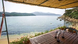 A wooden table with bird sculptures, a bamboo roof, and a view of a lake with mountains in the background. - APPARTAMENTO IL SOTTOMARINO - IL SOTTOMARINO (Portoferraio)
