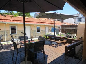 An outdoor patio with a table and chairs, a wooden deck, and a view of a building with a tiled roof.