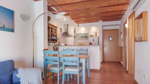 A cozy living area with a sofa, a dining table with chairs, a kitchen with a stove and cabinets, and a wooden ceiling.
