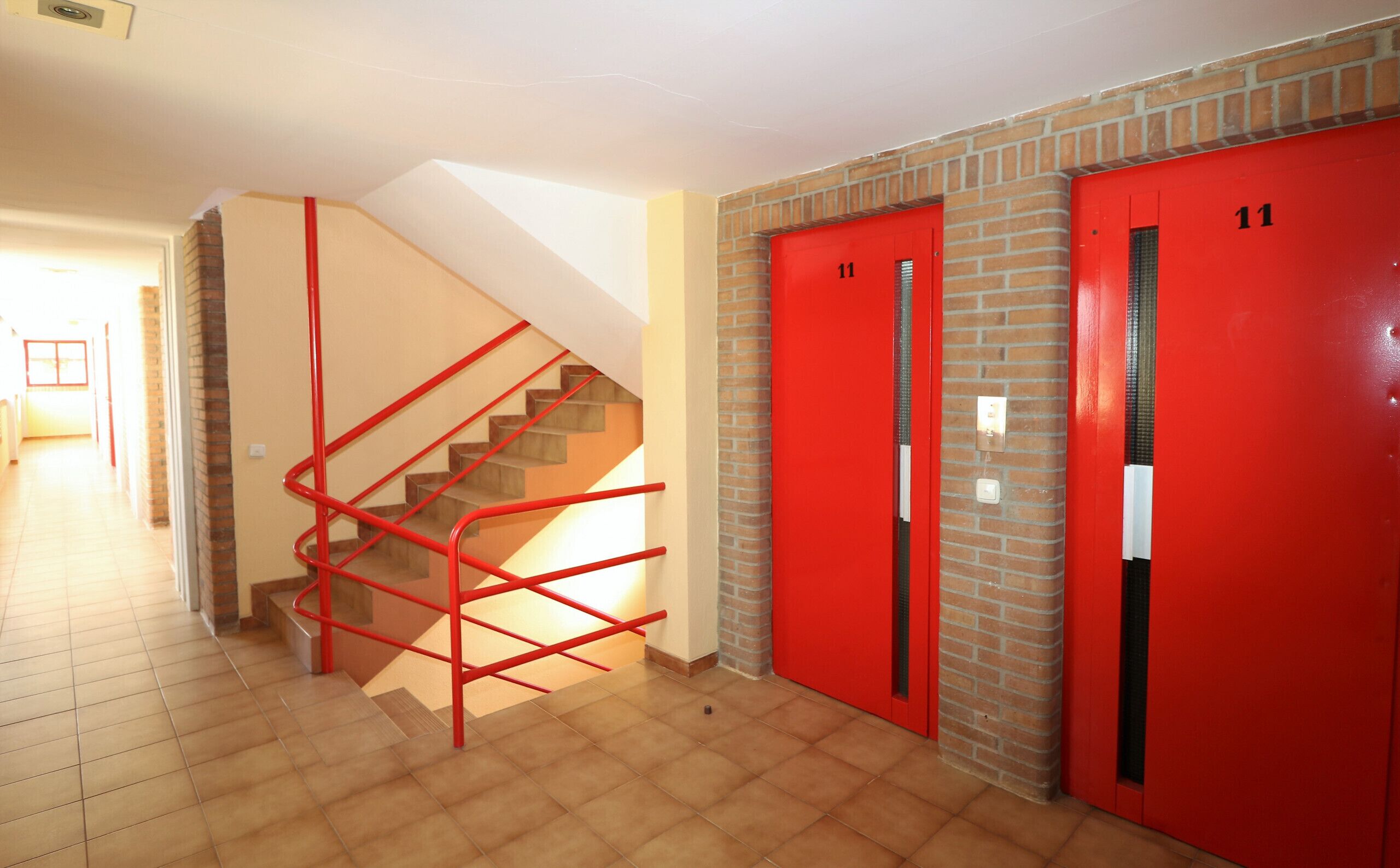 Un escalier avec des rampes rouges menant à une porte rouge portant le numéro 11.