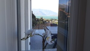 A view through a glass door of a balcony with a table and chairs, overlooking a lake and mountains. - Villa Mari, detached villa with magnificent garden view (Dervio)