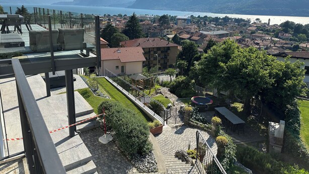 A residential area with a view of a lake and mountains. There are houses, a playground, and a paved area with stairs. - Villa Mari, detached villa with magnificent garden view (Dervio)