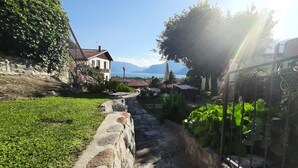 A stone pathway leading to a building with a view of mountains and a lake. - Villa Mari, detached villa with magnificent garden view (Dervio)