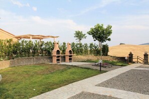 A courtyard with a pergola, two arched structures, a tree, and a stone wall.