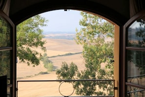 A view from inside a room with a large arched window overlooking a landscape with trees and rolling hills.