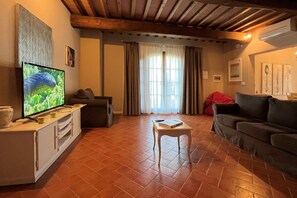 Ein gemütliches Wohnzimmer mit Fernseher, einer Couch, einem Couchtisch und einem Fenster mit Vorhängen.