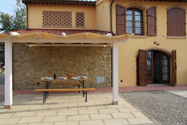 A covered outdoor dining area with a stone wall backdrop, a wooden table, and benches.