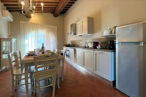 Una cocina con armarios blancos, una mesa de comedor con sillas, una lámpara de araña y un refrigerador.