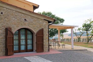 Edificio de piedra con un porche cubierto, una mesa con sillas y vistas al campo.