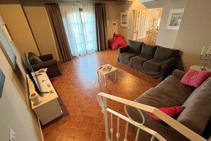 A living room with a sofa, a coffee table, and a TV. There is a staircase with a railing leading to another room.