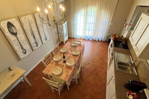 Un comedor con una mesa preparada para cuatro, un aparador con puertas de vidrio y una cocina con pileta y alacenas.