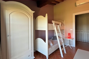 A bedroom with a bunk bed, a wardrobe, and a small table with a red lamp.