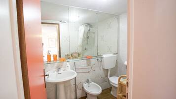 Une salle de bain avec une douche à parois de verre, un lavabo blanc, un bidet et des toilettes.