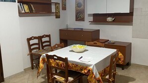 Un comedor con una mesa dispuesta para cuatro personas, rodeada de sillas de madera. Hay un ventilador de techo arriba y un armario blanco con un estante debajo.