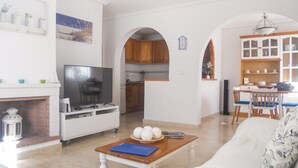 A living room with a TV, a fireplace, a dining area with a table and chairs, and a kitchen with wooden cabinets.