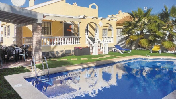 A swimming pool with a clear blue water, surrounded by a well-maintained lawn and palm trees.