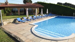 Une piscine entourée de chaises longues et de parasols, le tout bordé d’un bâtiment en briques doté de fenêtres en arc de cercle.