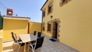 Une terrasse avec une table et des chaises, un bâtiment jaune et une petite cheminée en briques.