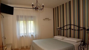 Une chambre à coucher avec un lit, un lustre, un téléviseur fixé au mur et un papier peint à rayures.