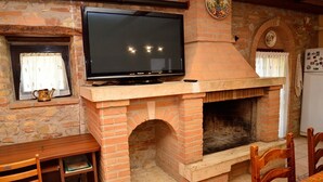 Une cheminée en briques avec un téléviseur fixé au-dessus, une table en bois et des chaises dans une pièce aux murs en pierre.