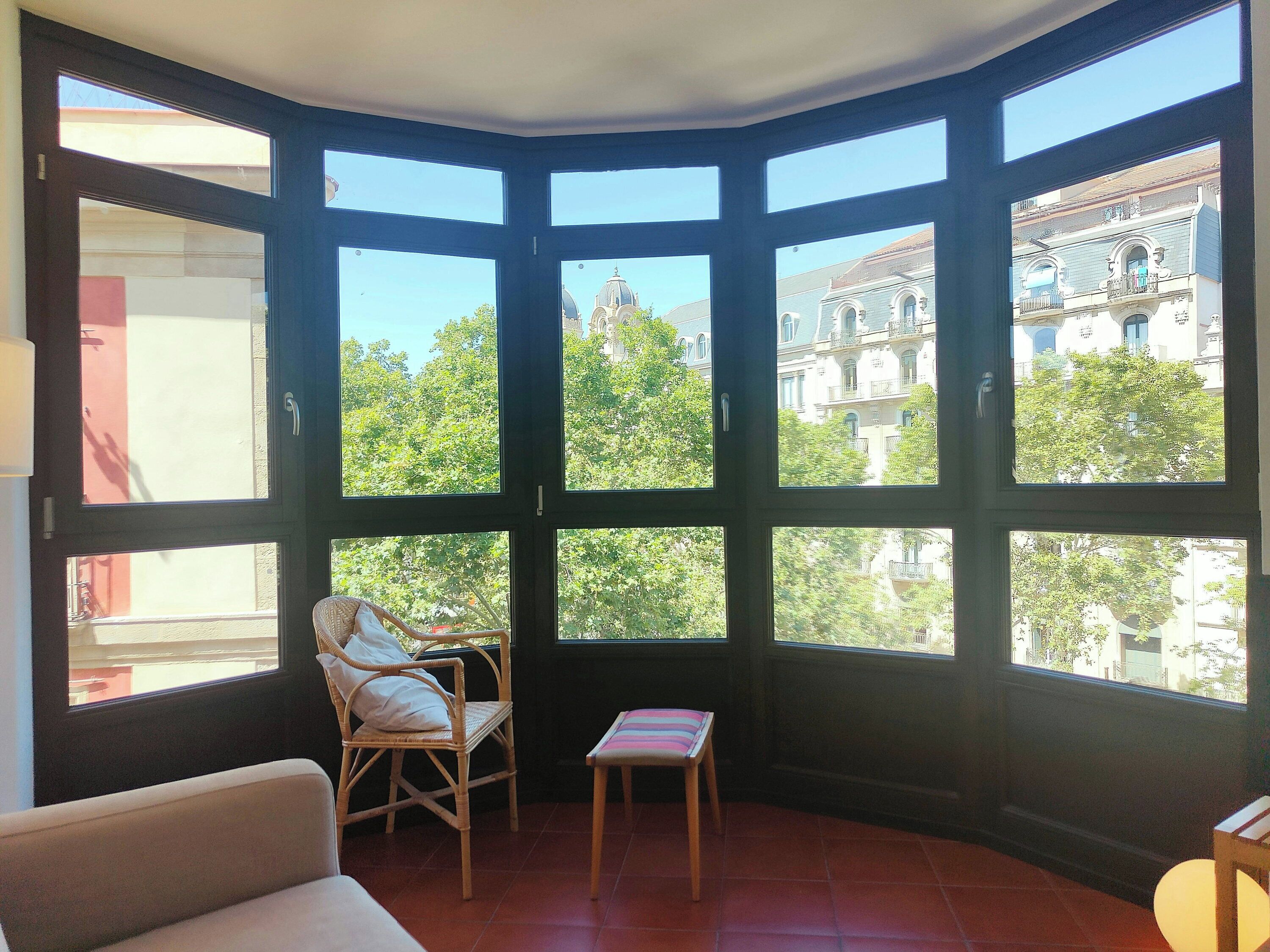 A corner room with large windows, a wicker chair, a small table, and a sofa.