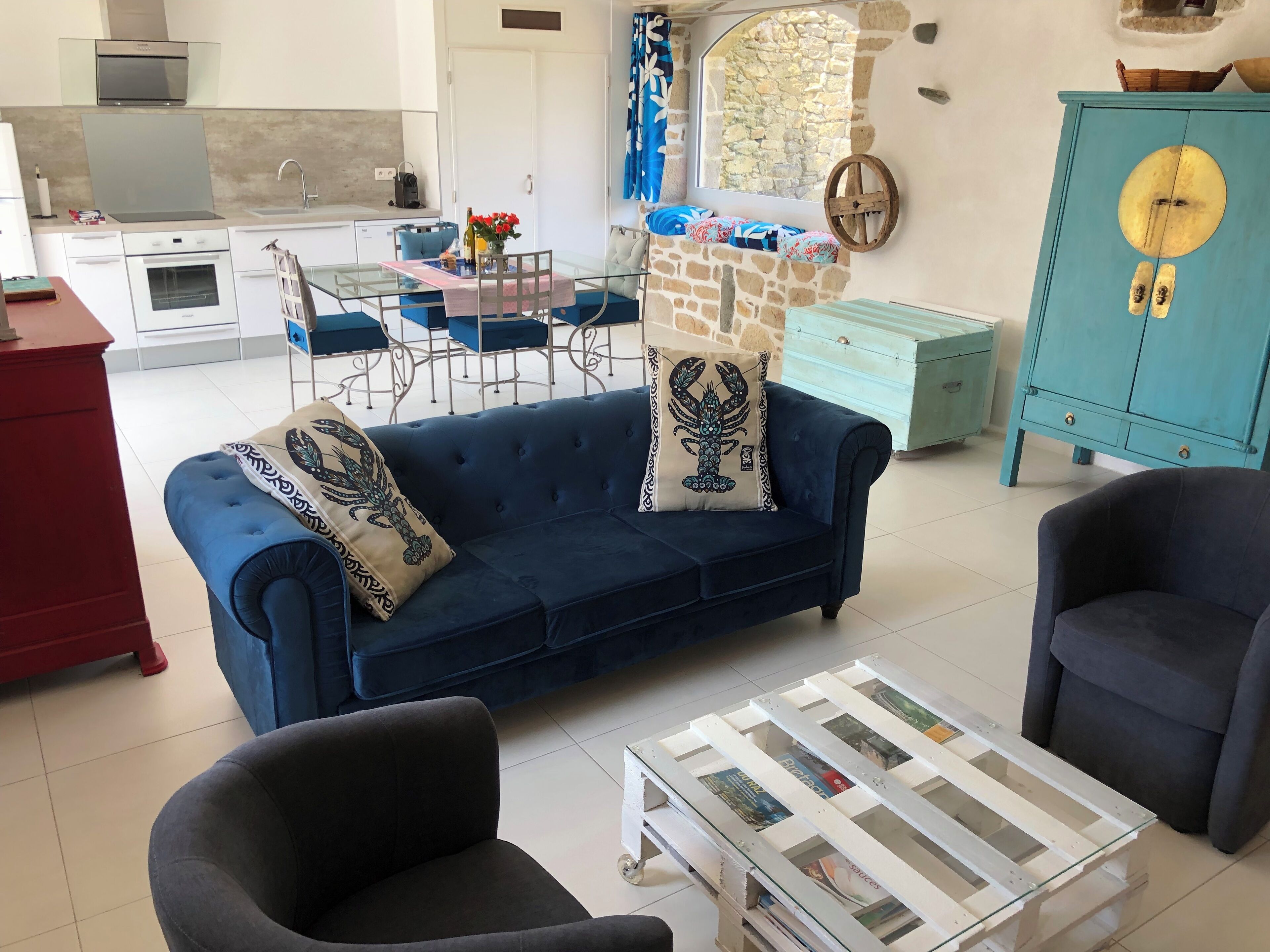 A modern living room with a blue sofa, two armchairs, a glass coffee table, and a stone wall.