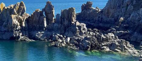 A rocky coastal landscape with clear blue waters and distant mountains.