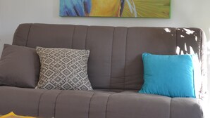 A living room with a brown sofa, patterned and solid blue cushions, a wooden coffee table with a magazine, and a large parrot painting on the wall.