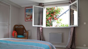 A bedroom with a bed, a chair, a window with curtains, and a radiator.