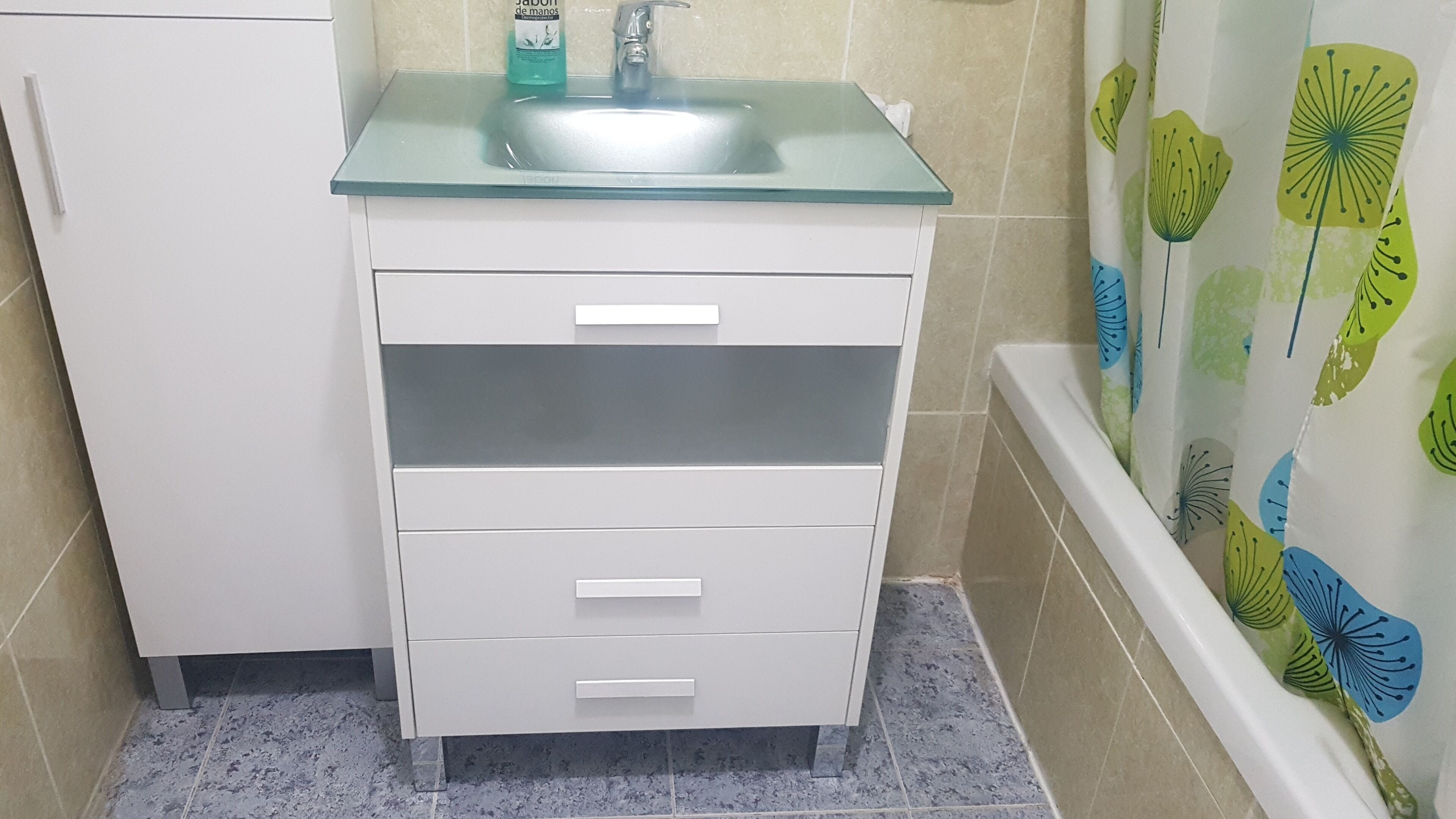 A bathroom with a white vanity, a glass sink, and a shower curtain with a leaf pattern.