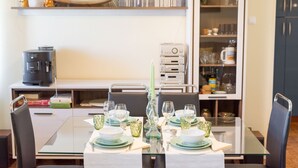 Een eethoek met een glazen tafel voor vier personen, omringd door stoelen. Op het aanrecht staat een koffiezetapparaat en een magnetron.