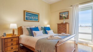 Een netjes ingerichte slaapkamer met een bed, nachtkastjes, een dressoir en een groot raam met uitzicht.