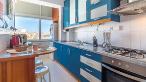 Een moderne keuken met blauwe kastjes, een gasfornuis en een uitzicht op de stad door het raam.
