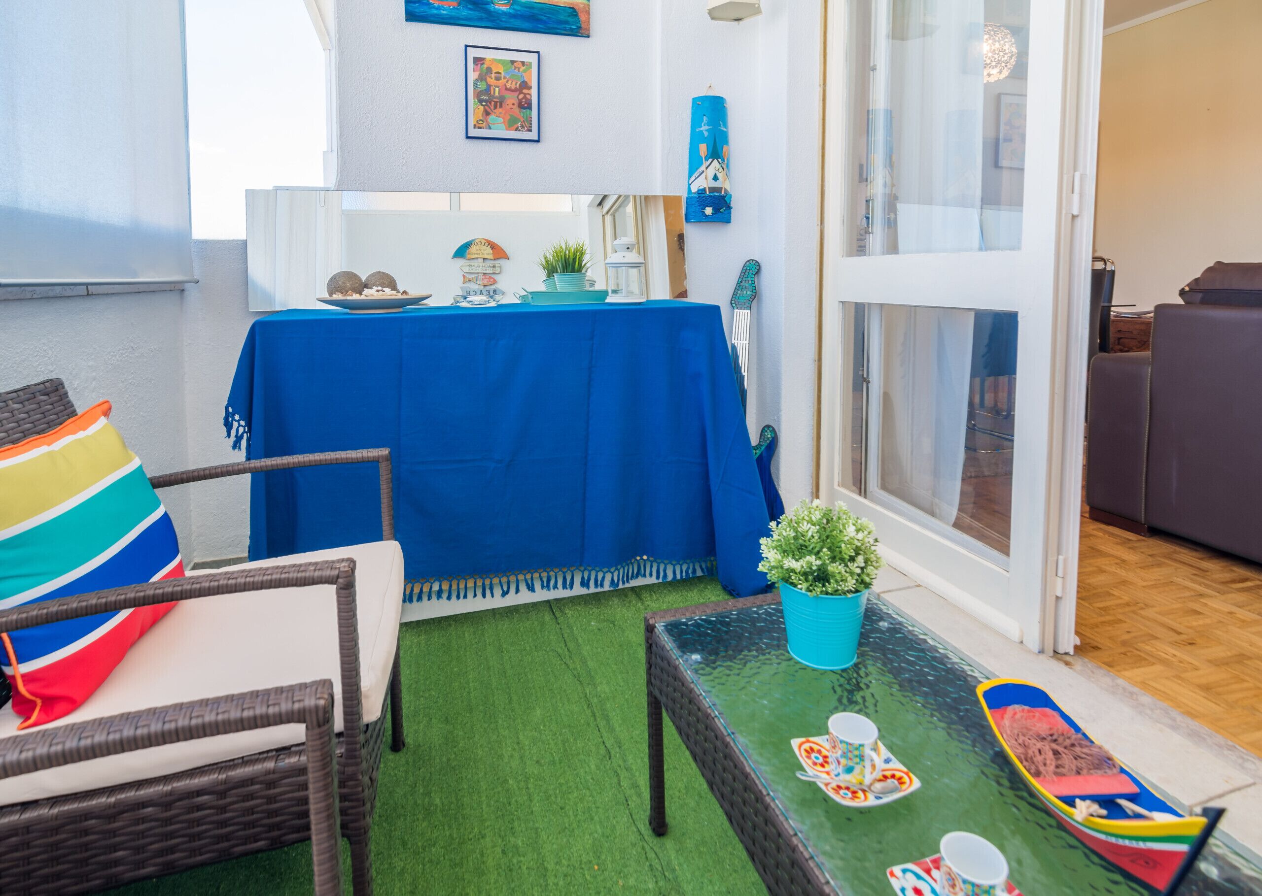 Un espace extérieur accueillant, aménagé avec des meubles en osier, une table bleue et une petite maquette de bateau.