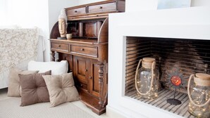 A cozy living room with a wooden sideboard, a fireplace with decorative jars, and a patterned throw over a sofa.