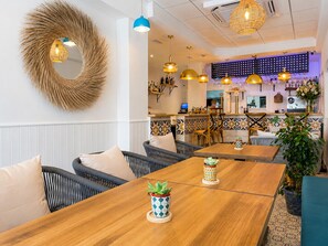A restaurant with wooden tables, wicker chairs, and hanging pendant lights.
