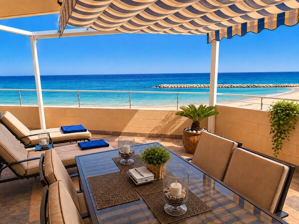A terrace with a view of the sea, furnished with chairs and a table, and a pergola overhead.