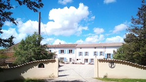 A white building with blue shutters, a gravel driveway, and a gated entrance.